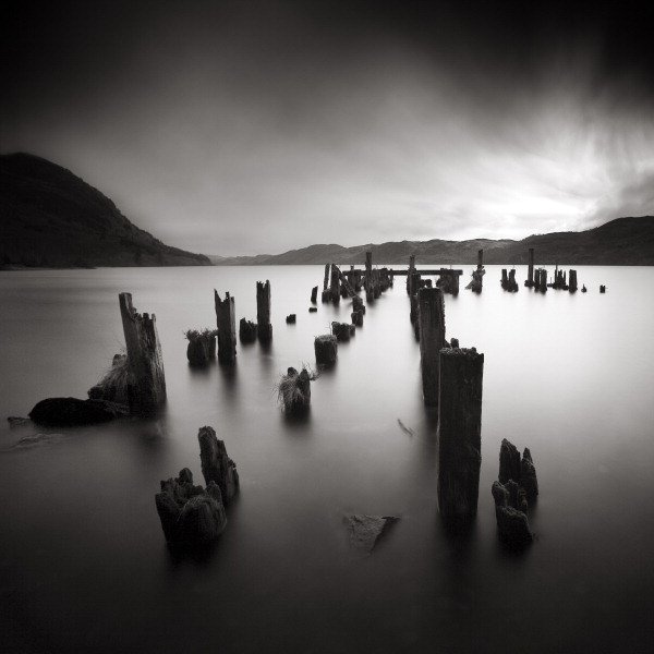 Carcass, photography by Denis Olivier. Loch Ness, Scotland, april 14, 2006.
http://www.denisolivier.com/p_sets.php?pid=936


It was my goal to go to this lake for this trip. I've always thinking of an isolated area, just with vans for mad scientists who were waiting for the Nessy. Despite of that, bunch of tourists and bus etc etc ... I can't find a proper place to shot. The access is not simple, and for the most common ones, there's was too much people, even in April. Finally while driving near the shoreline, I saw several meters under the road this old pier. My monster was found! After trying to go back to found it, I went through the forest near the shore. There was many carcasses, but from cars. Very strange area, no one here and all the haunting legends about it. I can't access without putting my shoes in the lake, too dangerous with all this metal for my feet. I finally place the tripod in the lake, me also, and try to deal with the low light around and the cold water. I took 3, this one was my selection.

I've asked many people what was this pier name and history but I still don't find anything about it at this time.

New 2010 edition.. Canon 5D, Canon Zoom 16-35L. In Nature, Scenery, Waterscape