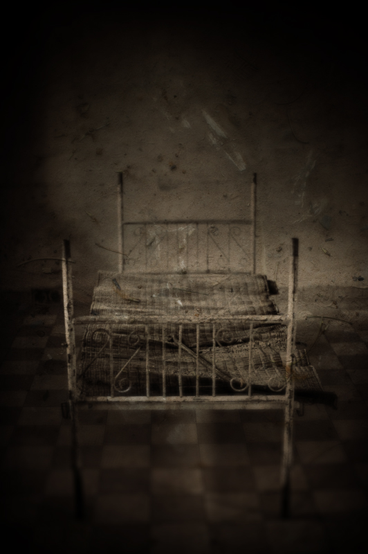 S-21, photography by Mark Hamilton. A combination of two images. The base image a picture of a prisoners bed in a torture cell in Tuol Sleng and above it an image of the earth at the killing fields just outside of Phnom Penh. The two sites are inseparable.. Canon EOS 1Ds MkII   Canon EF 50mm f1.2L. In Construction