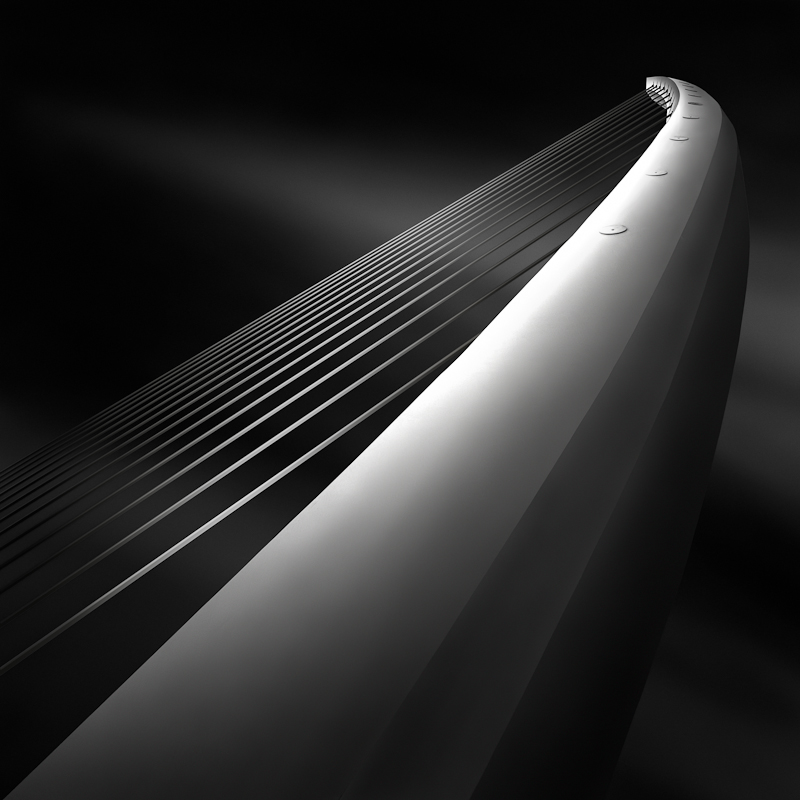 - International Photography Awards IPA 2012 - Honorable Mention -

This is the third image from my study  of the Katehaki Pedestrian Bridge in Athens, design by Santiago Calatrava.
I have to say that this study is one of the most complex works I've done in photography up to now. Very challenging for many reasons. The place and the surroundings are very crowded and construction cluttered so it's quite difficult to find clean angles to shoot and almost impossible if you intend to obtain an abstract look and keep the "streety" elements out of the frame. Then, one has to work with wide enough angle to be able to deal with the narrow spaces that constrain the perspective. Then, the deck of the bridge is wooden and there are a lot of pedestrians using the bridge, so it's almost impossible to shoot there during the day (I also have some night shots taken there and the first image in the series, like a harp's strings I,  is actually a night shot). There is only a narrow band of concrete floor where you can place your tripod, but even so, people are passing by and one: you bother them, two: they bother you. Plus they are curious and ask a lot of questions, which is not exactly bad, but keeps you from doing your job and you might lose precious clouds like this  :). Then the processing was  quite challenging too. Being a complex volume, with accentuated curves and a lot of cables going up and down, plus the stairs, the handrails and other elements that can be seen in a wider perspective (as the number II of the series - the "sister" of this one here) you have to hierarchize very well the image and the elements within in order not to get a cluttered one with no point of interest or with too many. That means you have to look very carefully at your composition, trying to keep it as clean as possible, and then you have to  play with light and is intensity and try to give the right amount of care to each element so to match your vision of the object and convey  the feeling you have in mind. I found none of these images easy to process up to now. Every one of them was a different challenge, even if some seemed easy to be worked with in the beginning. The selections in all of them were completely crazy, these cables can drive mad the most patient person, I'm telling you. The skies also were tough to get right with all these things going on in each photo of this study.
But all in all, I loved working on it (and I still do, as it's an ongoing series). I've learned tons of things struggling with these images and I think this was the best LE exercise I could do to be able to gain confidence in my skills and try even more complex approaches the next time.. Nikon D7000. Long exposure. Like A Harp's Strings III - Rising, image by Julia Anna Gospodarou. Image #390716